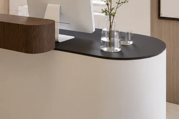 The curved end of the reception desk: a white front, a black worktop and a raised dark wood counter section