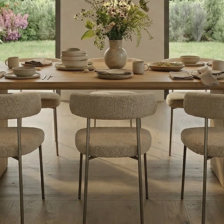Rounded dining chairs upholstered in bouclé at the wooden table, with matt ceramic tableware and a bunch of flowers