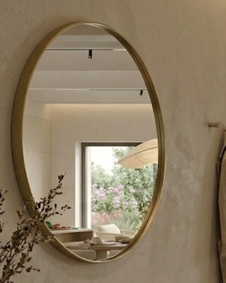 Round mirror with a thin metal frame on the textured wall, reflecting the dining area and the garden