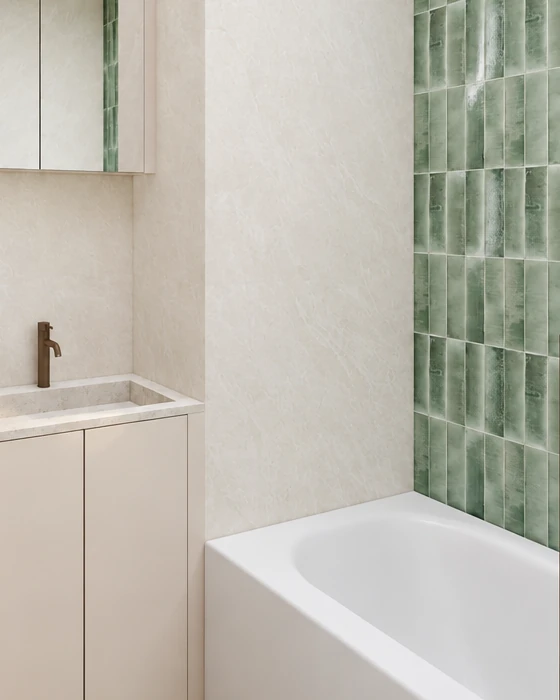 Green glazed rectangular tiles laid vertically in a band behind the bath, beside them light stone-effect wall cladding, and on the left a vanity top with a bronze-coloured tap