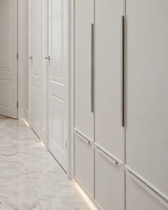 Tall white built-in cupboards with long handles and concealed plinth lighting beneath them, above the marble-effect floor