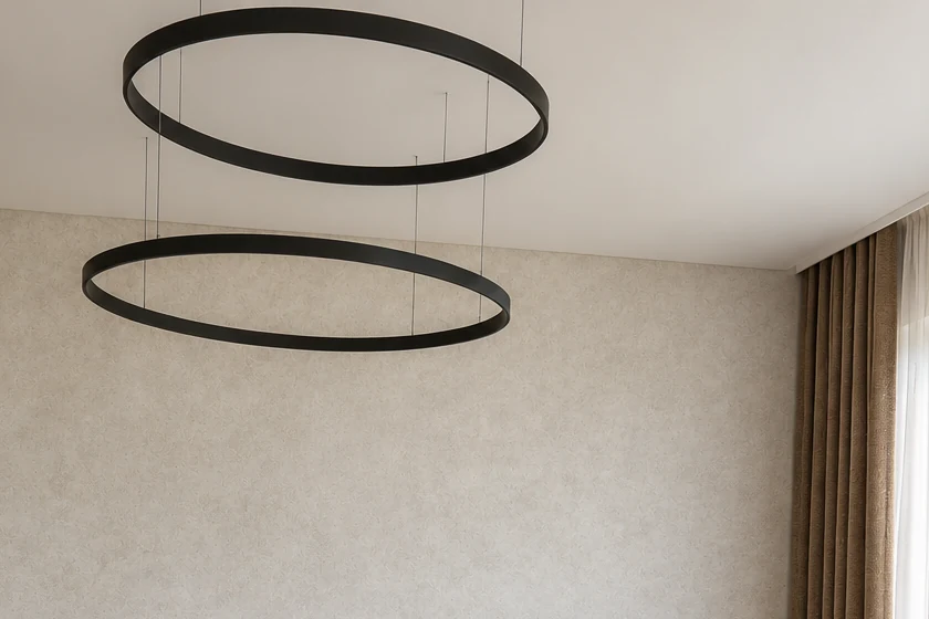 Pendant light made of two black rings at different heights, with a light, textured wall and a floor-length curtain in the background