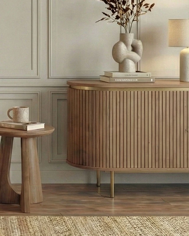 Fluted wooden chest of drawers on slim brass legs, with a round wooden side table beside it and framed wall panels behind