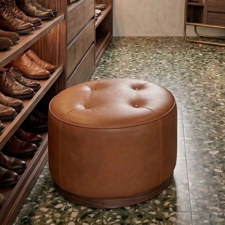 Round, buttoned cognac leather pouffe in the middle of the walk-in wardrobe, with open walnut shoe shelves and terrazzo flooring around it