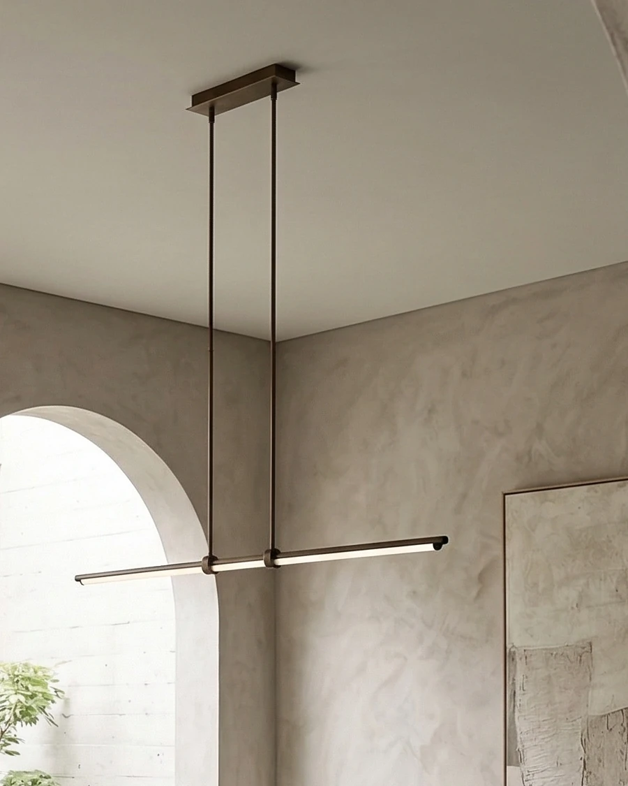 Slim, modern brass linear pendant above the dining area, with an arched opening and textured wall finish in the background