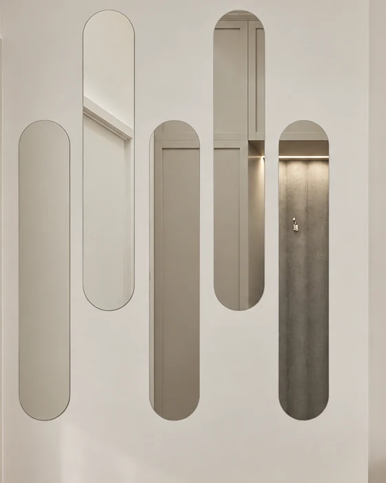 A group of capsule-shaped wall mirrors in the entrance hall, reflecting the seating niche and the wardrobes