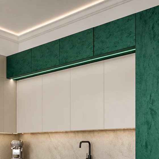 Deep green upper cabinet fronts with a marbled finish, a light strip and a run of light cabinets below them, and a moulded cornice with concealed lighting above