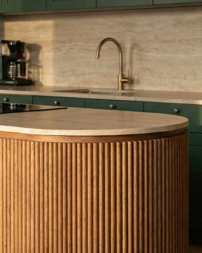 The curved end of the kitchen island with fluted wood cladding and a travertine-effect worktop, a brass tap behind it