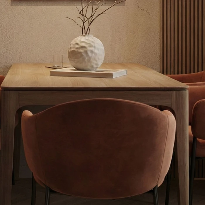 Curved backrest of a terracotta velvet chair, with the wooden dining table and a white ceramic vase behind it