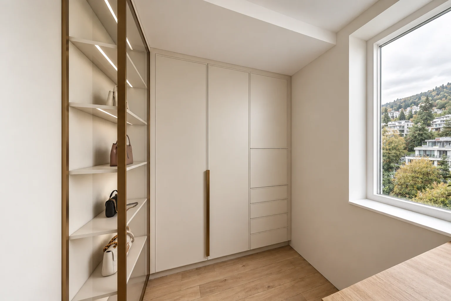 Walk-in wardrobe with a full-height pale beige built-in cupboard with a long gold-bronze handle and drawers, a gold-bronze-framed lit shelving unit on the left and a large window on the right