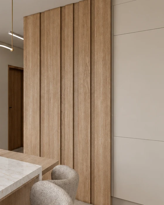 Oak slatted wall cladding beside the pale beige high-gloss bank of kitchen units, with the corner of the marble-effect island and upholstered chairs in front