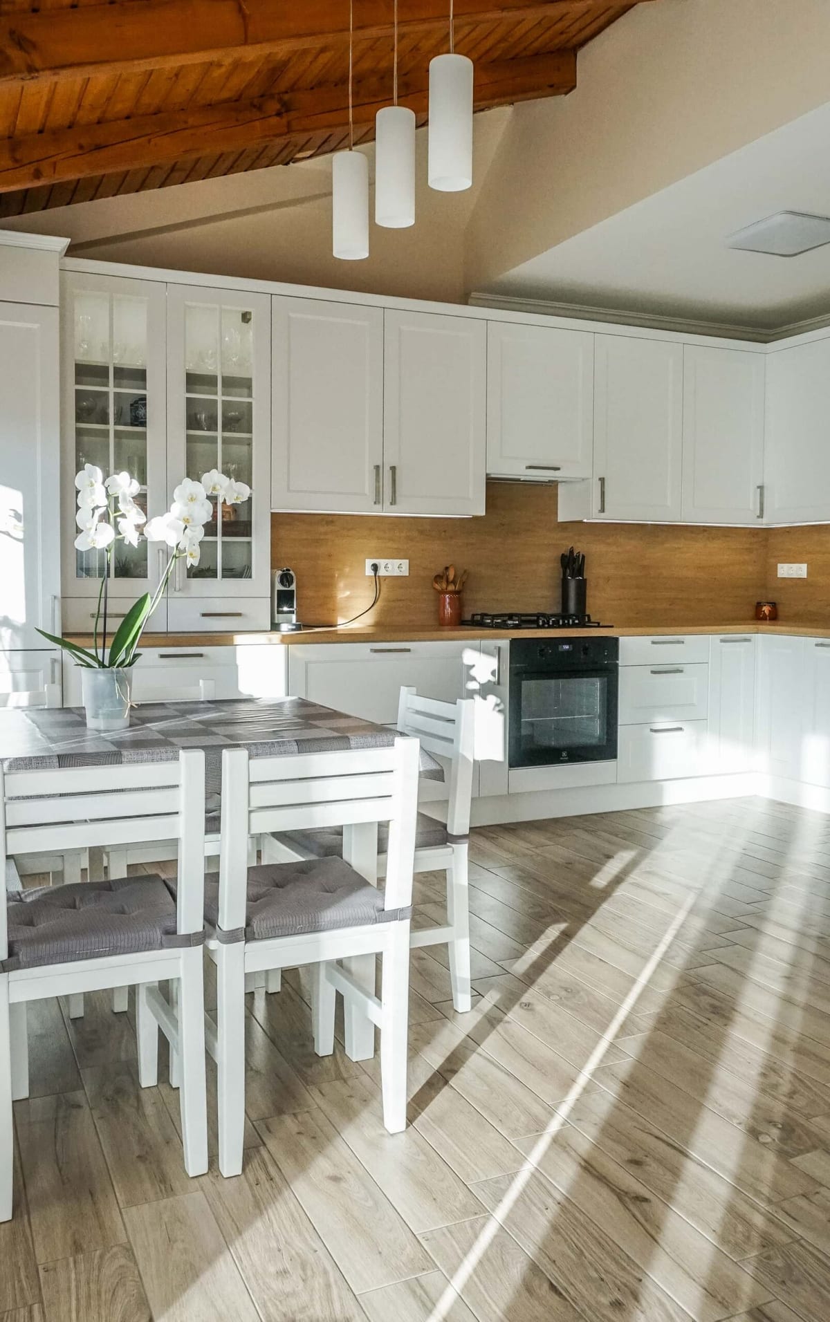 White framed-front kitchen with wooden worktop beneath an exposed timber-beam ceiling